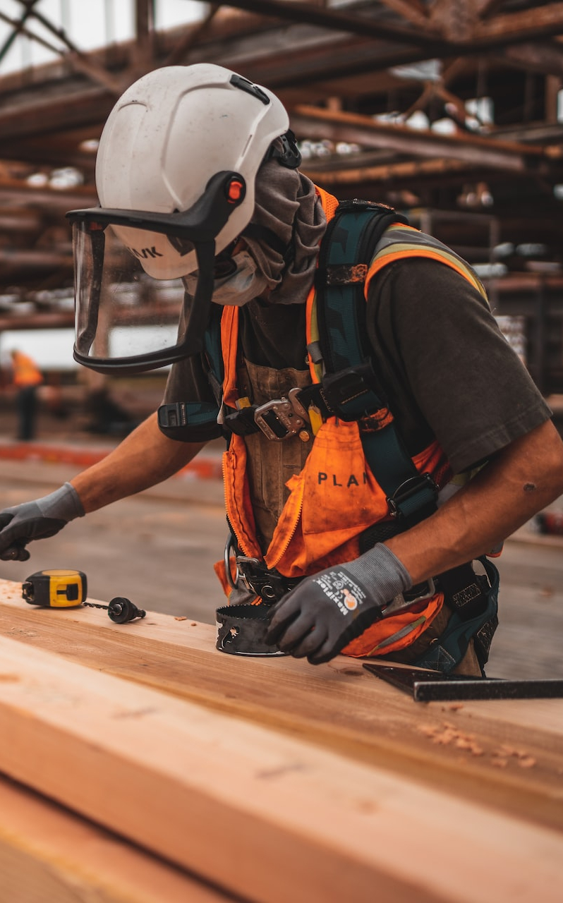 man in orange and black vest wearing white helmet holding yellow and black power tool